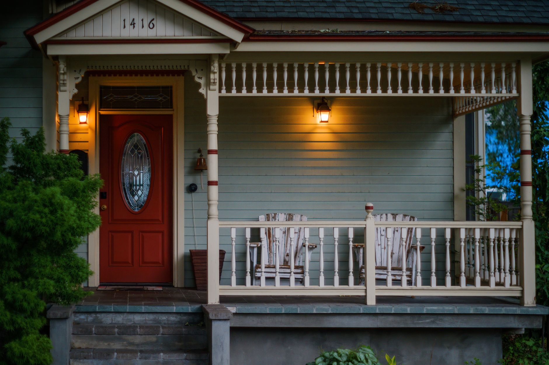 Front porch of a home with a red door and lit sconces in the evening
