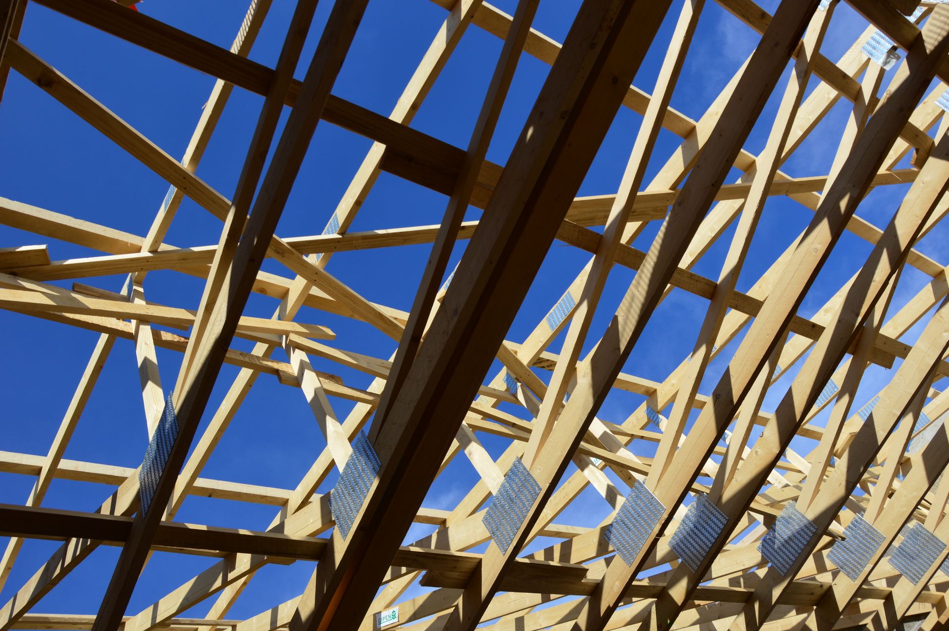 Roof truss framing seen from below against a blue sky